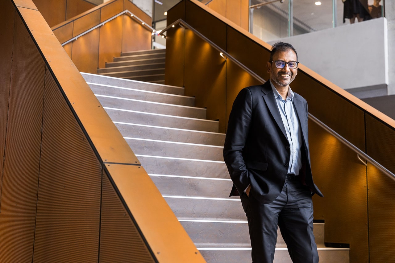 Professor Sarath Ranganathan looks into the camera and stands on the inside staircase inside the Aikenhead Centre for Medical Discovery building