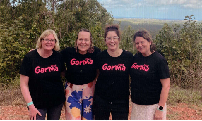 Amanda Currie, Ellen Hewitt, Kellie Henderson-Giles and Janine Sala pose together at the Garma Festival. The background is bushland with a partial view to a shrub-like plain below.