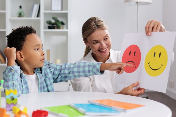 A child points to a happy face drawing held by a woman.