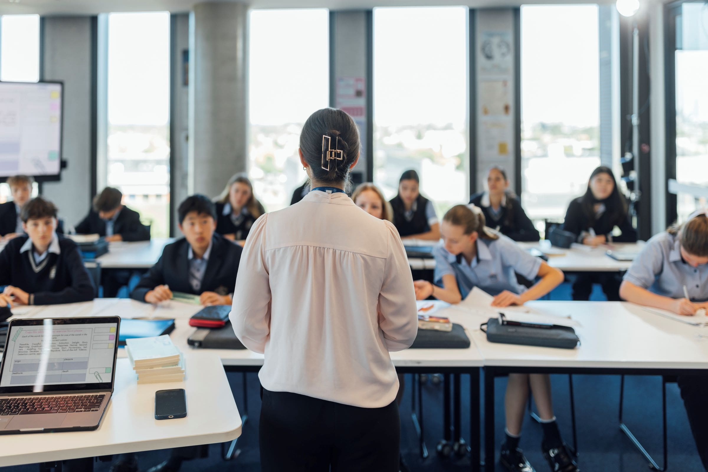 A teacher, whose back is to the camera, addresses a classroom of Australian secondary school students
