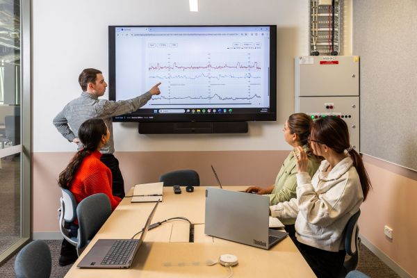 Emerson Keenan standing in front of a display and pointing at foetal and maternal heart rate readings. His team are seated at a table and listening to his presentation