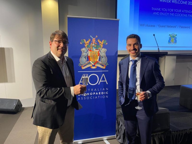 Nicolas Sclavos and Associate Professor Erich Rutz, each holding a glass of wine, pose together at the Australian Orthopaedic Association Victoria and Tasmania Winter Welcome.