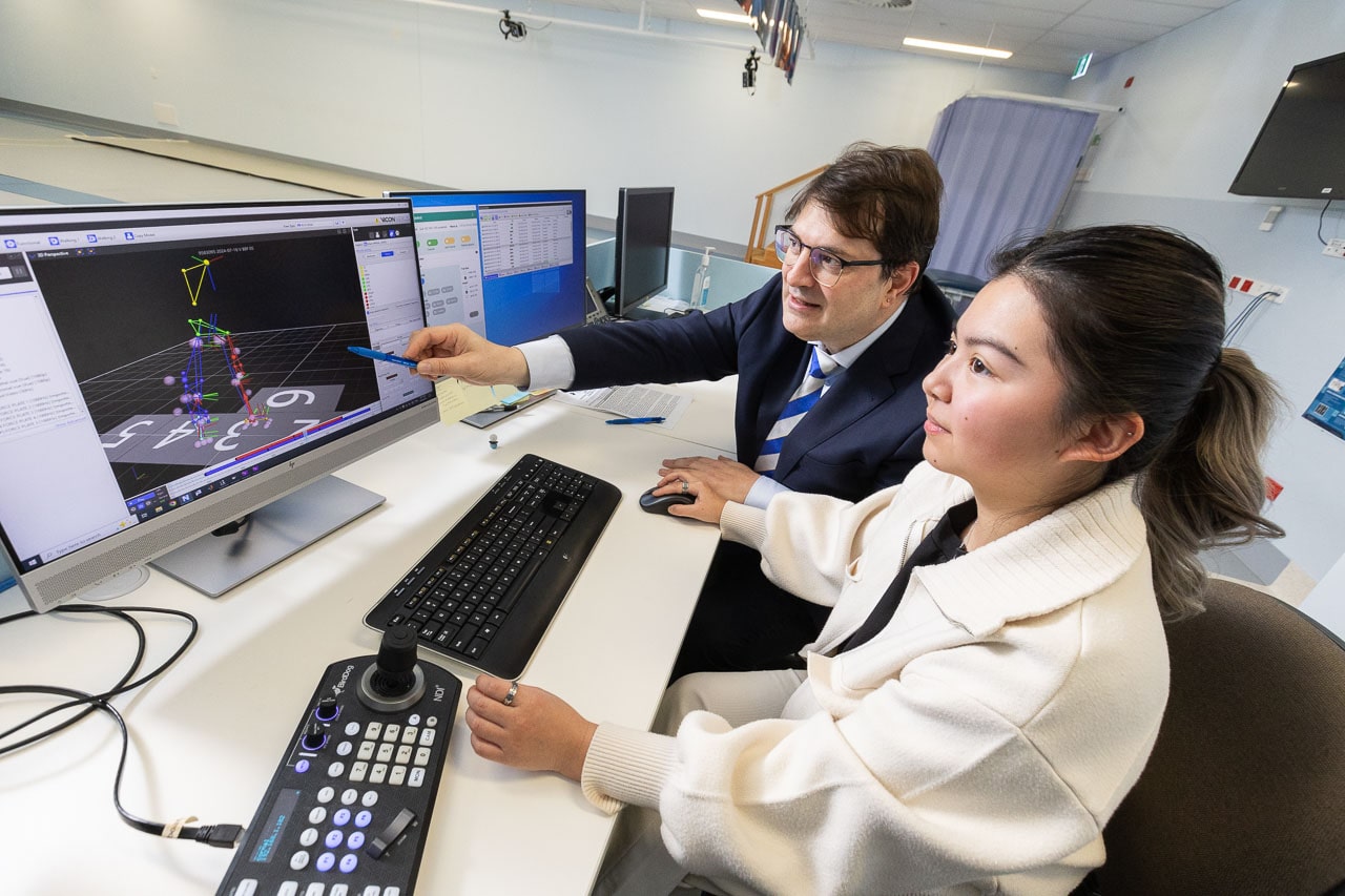 Associate Professor Erich Rutz, sitting at the back, and biomedical engineer Jinella Lopez, sitting at the front, analyse a colourful 3D skeletal model on the computers of the Hugh Williamson Gait Analysis Laboratory at the Royal Melbourne Hospital. Erich points at the model with a pen