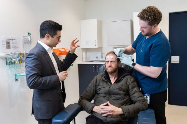 L-R Professor Piero Perucca and EEG scientists Kaelasha Tyler and Chris Farrell demonstrate how to perform an EEG. Kaelasha is being fitted with circuits to measure electrical activity from the brain