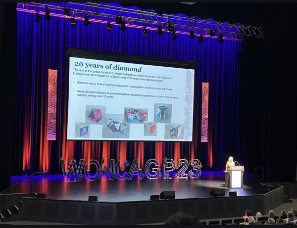 A presentation at a conference. The stage has a sign that reads 'WONCAGP23', projected onto a screen is '20 years of diamond'.